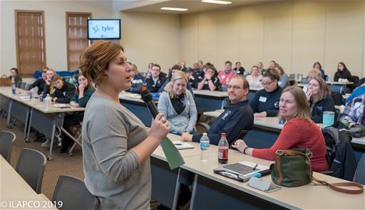 Woman holds microphone and speaks to seated crowd